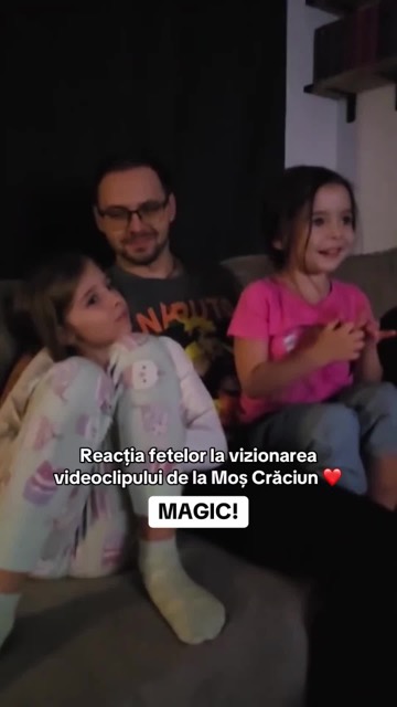 Două fetițe și tatăl lor urmăresc pe canapea videoclipul de la Moș Crăciun