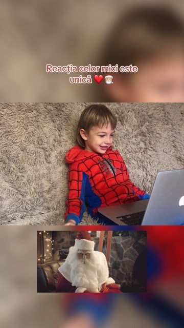 Un băiețel în costum de Spider-Man râde în fața laptopului cu Moș Crăciun pe ecran